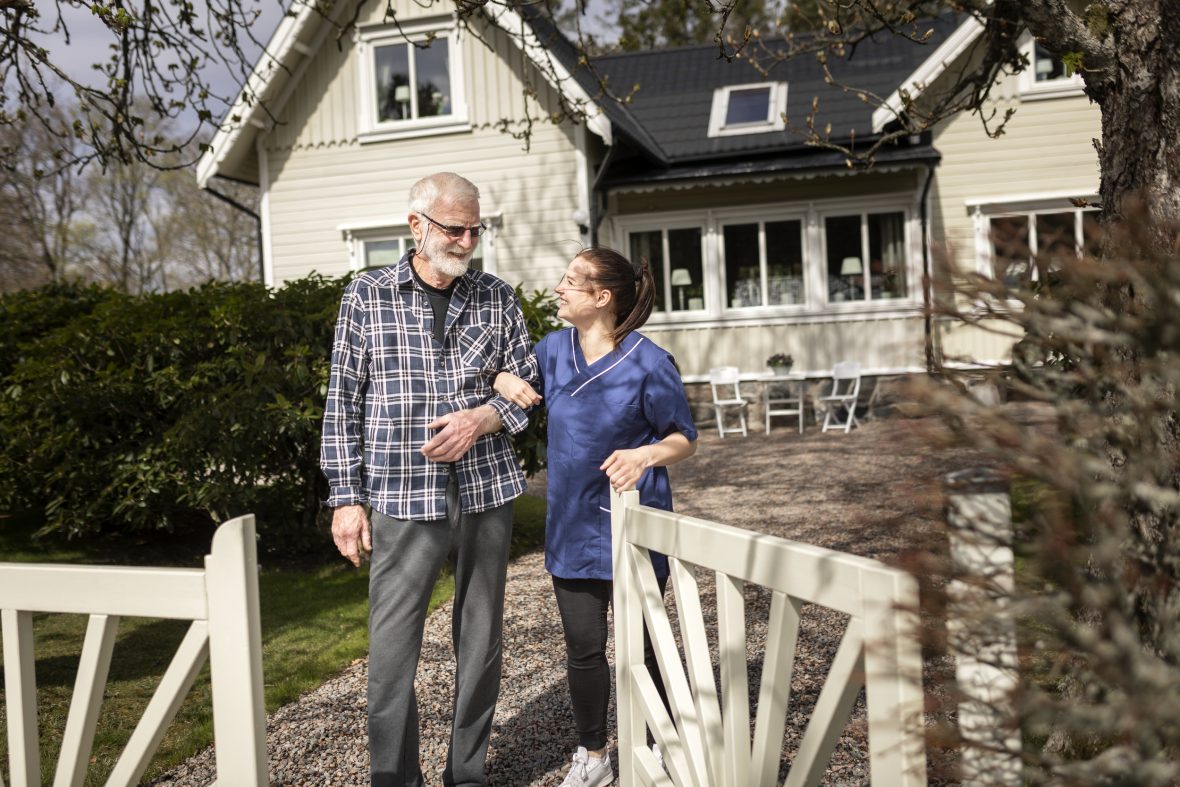 Kvinnlig hemtjänstpersonal hemma hos äldre man och tar promenad